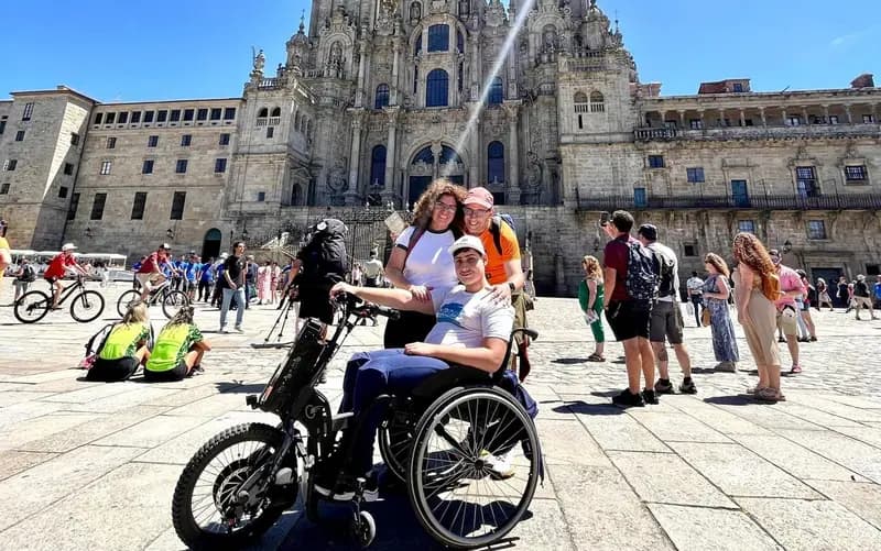 Un usuario de silla de ruedas posa con sus padres frente a la Catedral de Santiago de Compostela