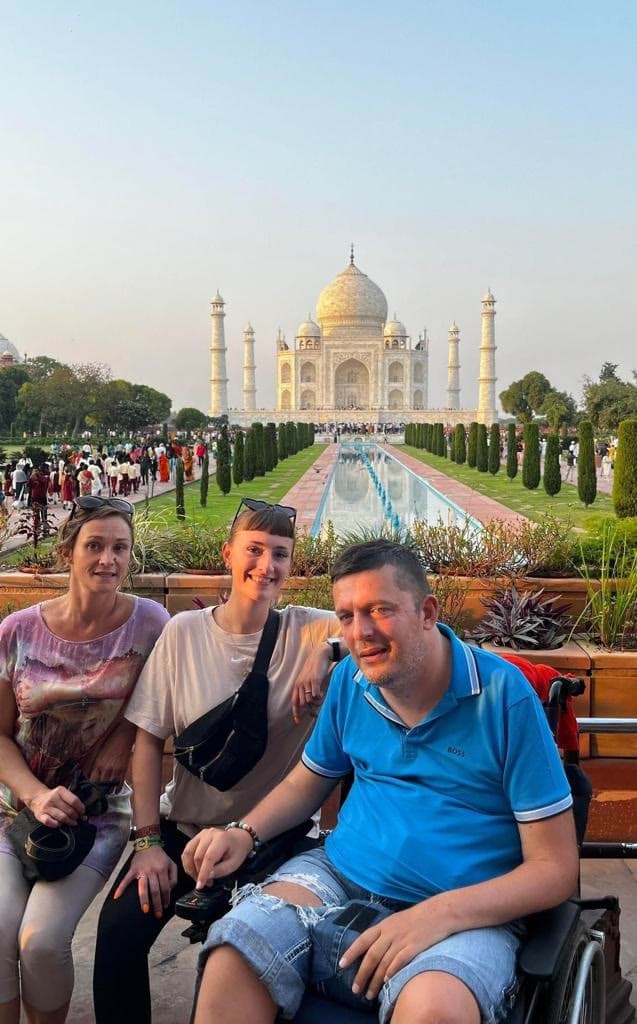 Un viajero en silla de ruedas y dos acompañantes, en los jardines del Taj Mahal, en la India.