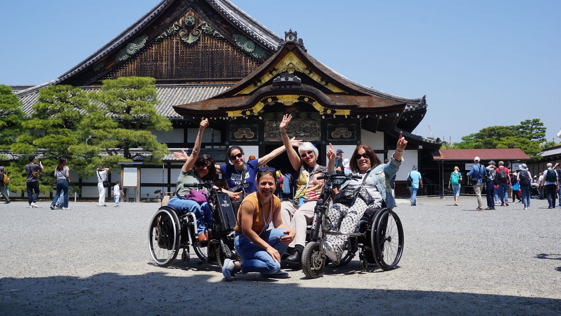 Un grupo de viajeros, varios en silla de ruedas, celebra con los brazos en alto delante de un castillo japonés.