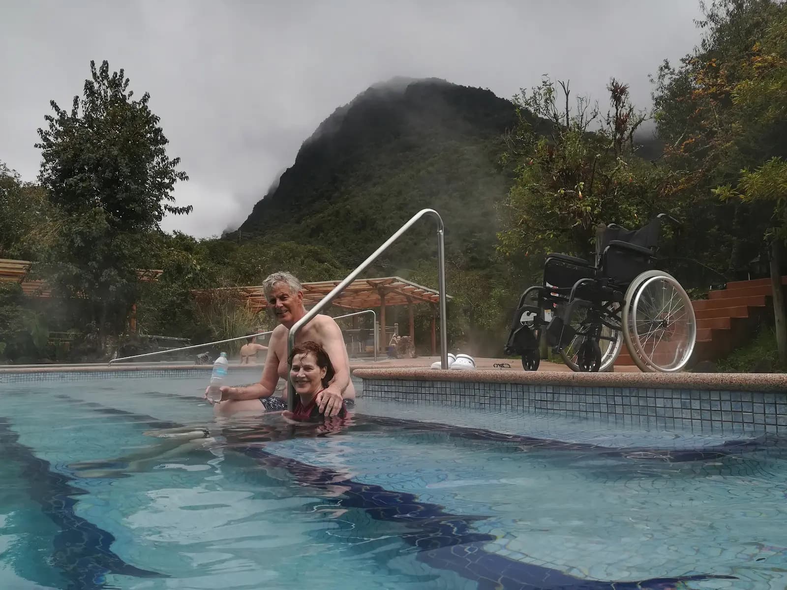 Una viajera entra en las termas de Papallacta, en Ecuador, por una rampa con barandilla; su silla de ruedas espera junto a la piscina.