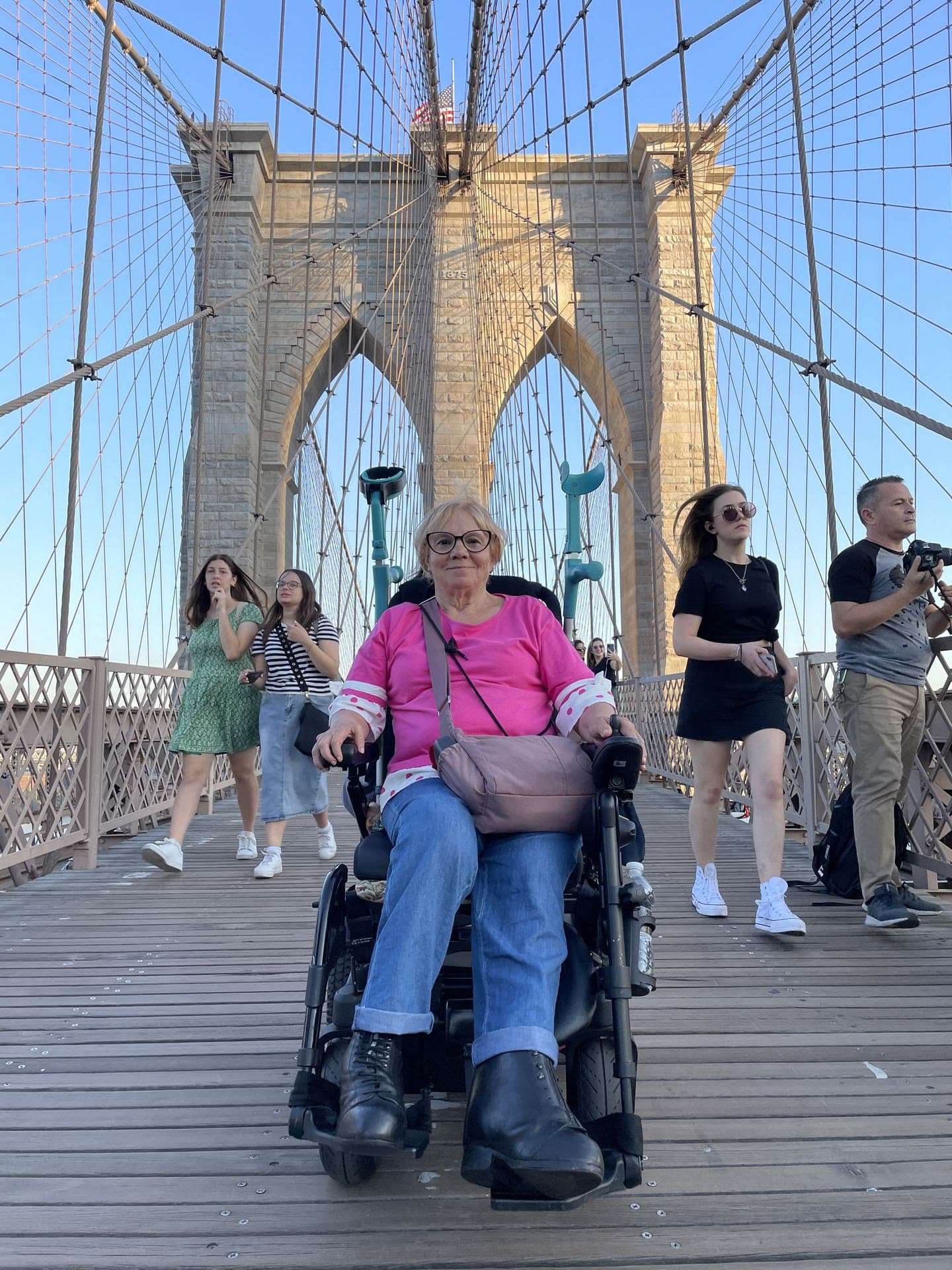 Una viajera en silla de ruedas eléctrica, con su grupo, en la pasarela del puente de Brooklyn, en Nueva York.