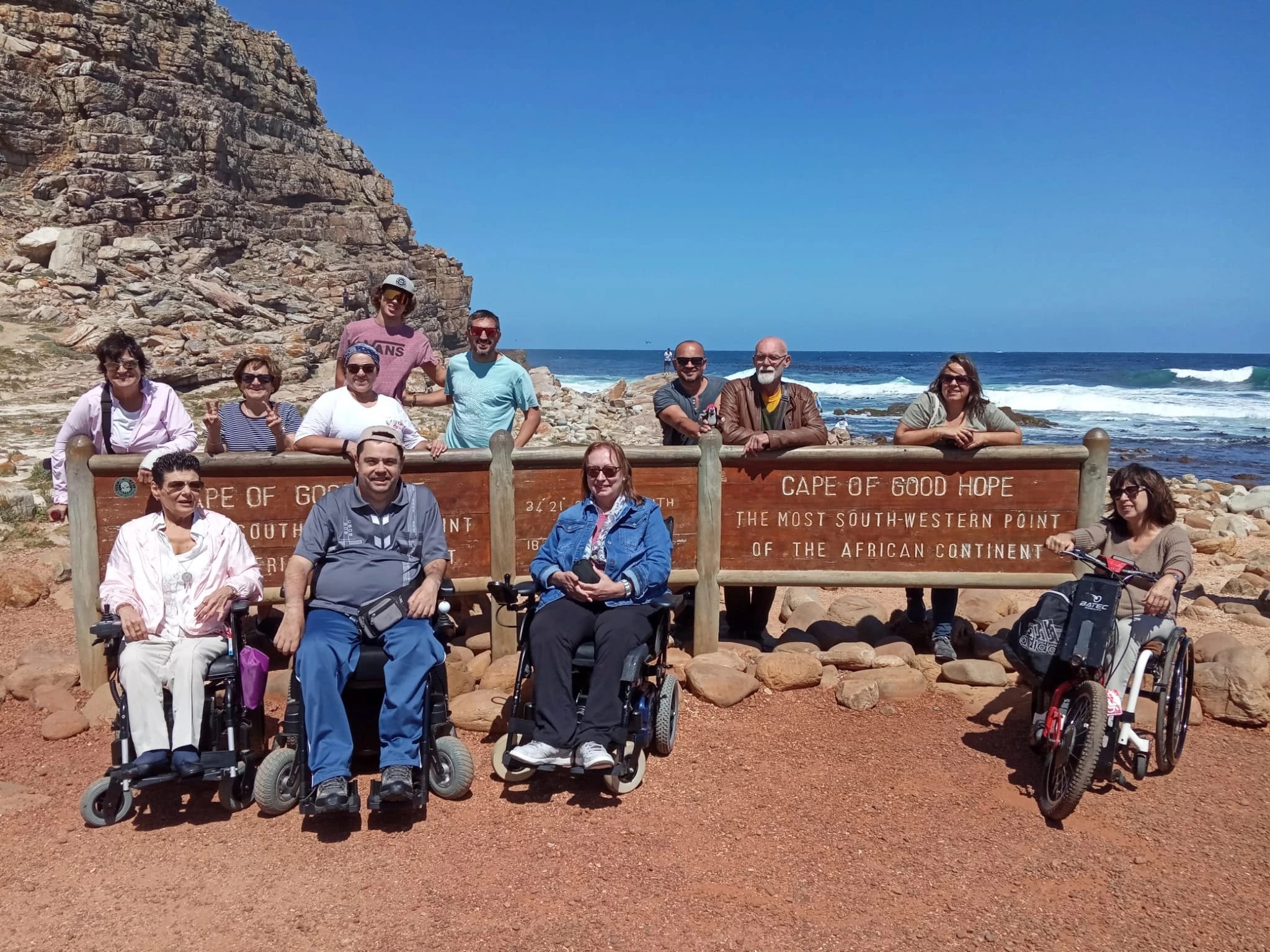 Un grupo de viajeros, varios en silla de ruedas, junto al cartel del Cabo de Buena Esperanza, en Sudáfrica.