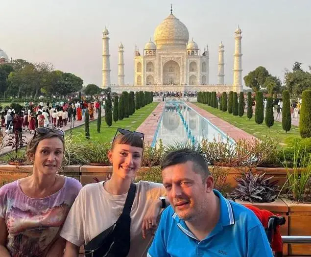 Un usuario de silla de ruedas con sus dos acompañantes de viaje en un monumento en India