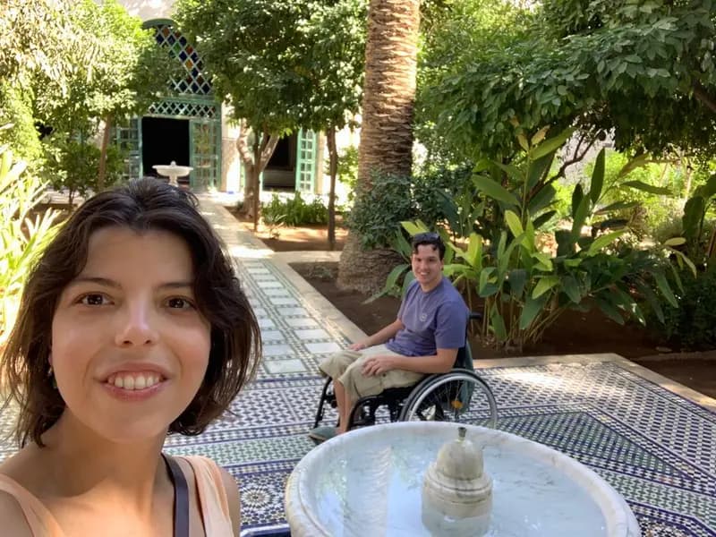Una selfie con una chica en primer plano y un usuario en silla de ruedas al fondo en un patio de un alojamiento en Marrakech