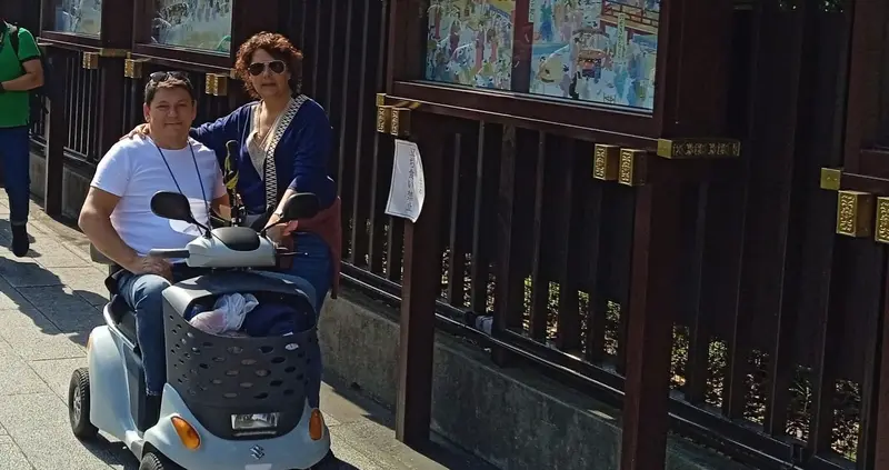 Una pareja, uno de ellos sentado sobre un scooter, posando frente a un monumento en Japón