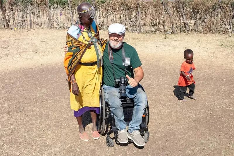 Usuario de silla de ruedas posando en un poblado Masai con una mujer y un niño jugando