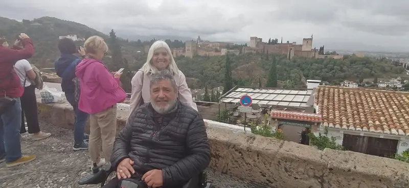 Un usuario de silla de ruedas con su esposa y al fondo la Alhambra