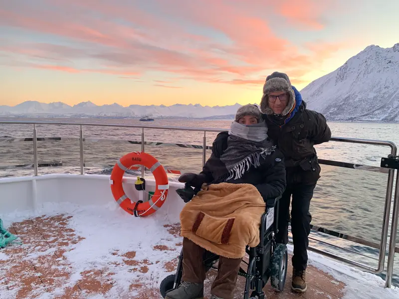 Dos viajeros, uno usuario de silla de ruedas, desde la proa de un barco con nieve durante una navegación en el fiordo de Tromso