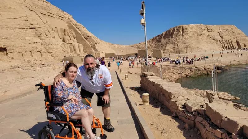 Una pareja en un viaje accesible a Egipto. Ella es usuaria de silla de ruedas. Al fondo se ven monumentos de piedra