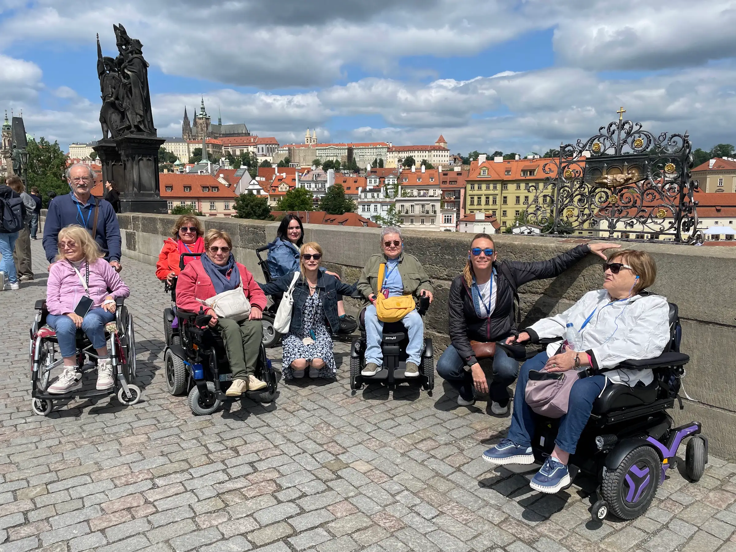 Un grupo de viajeros de Travel Xperience, varios en silla de ruedas, en el Puente de Carlos con el castillo de Praga al fondo.