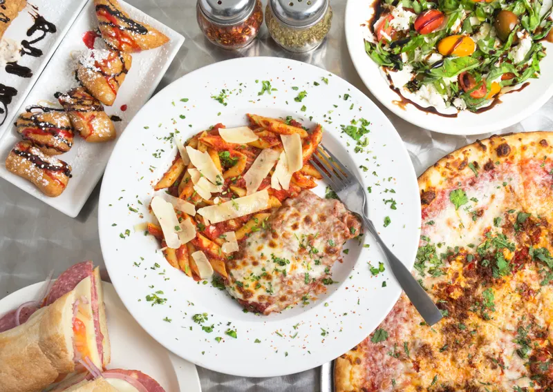 Gastronomía sin barreras en Italia accesible. Imagen de un amesa con un plato de pasta al centro, una pizza a su derecha y varios platos de comida en un segundo plano.