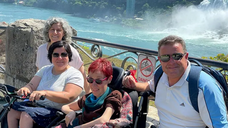 Dos personas usuarias de silla de ruedas junto a su familia en un mirador accesible frente a las Cataratas del Niágara