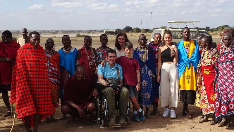 Un viajero con movilidad reducida rodeado de su familia y habitantes de un poblado Masai en un viaje accesible a Kenia.
