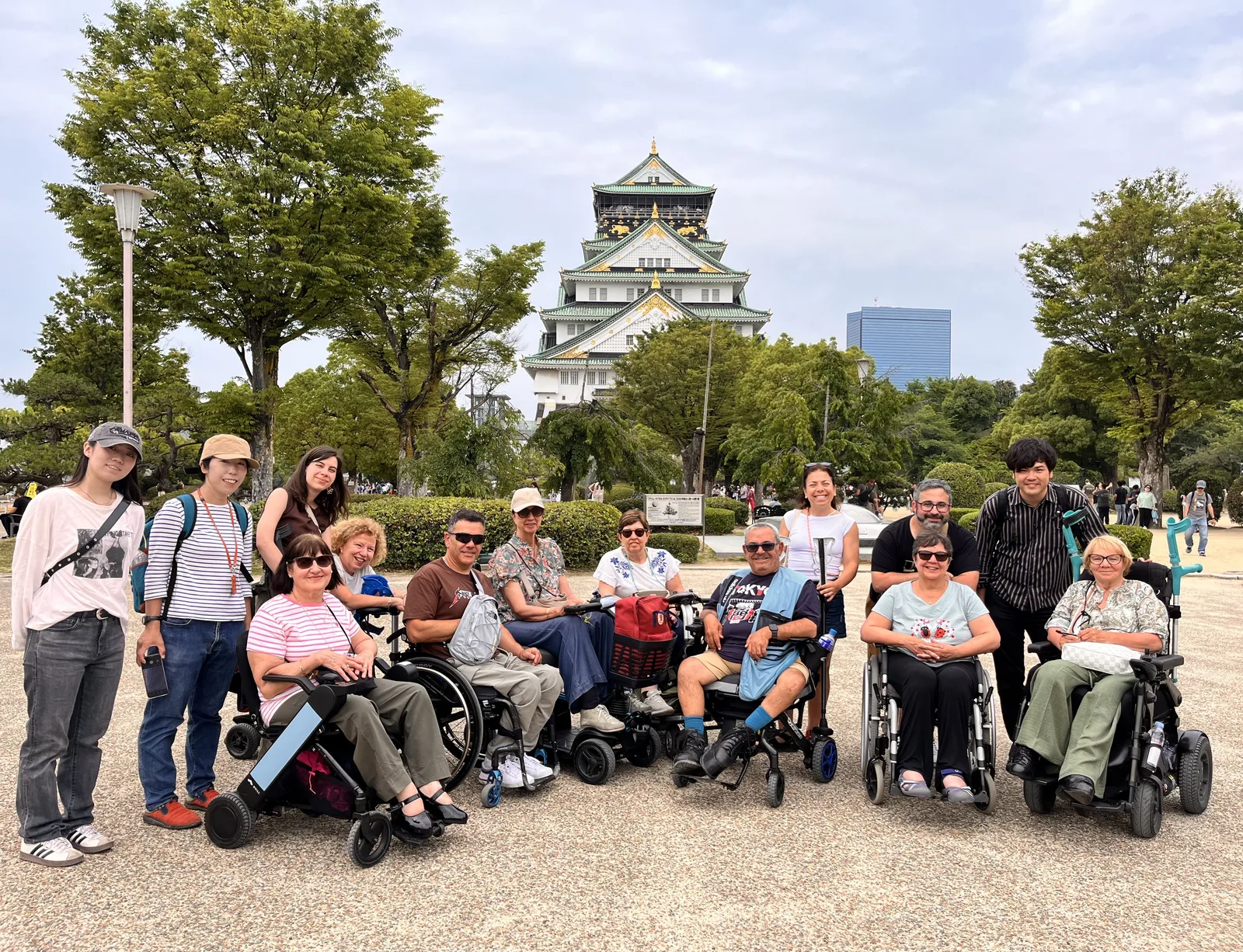 Grupo de turistas con sillas de ruedas en plaza frente a castillo histórico. Personas de diferentes edades disfrutando del lugar.