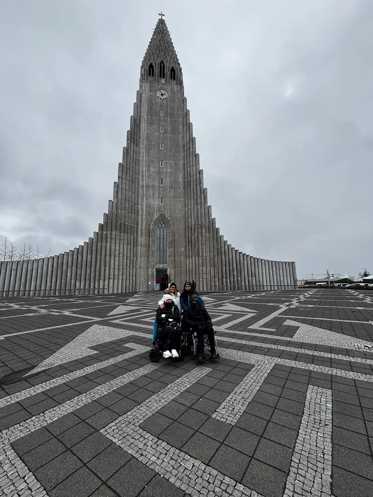 Iglesia de Hallgrímur en Reikiavik con fachada de piedra blanca, plaza pavimentada, personas de espaldas observando la arquitectura icónica.